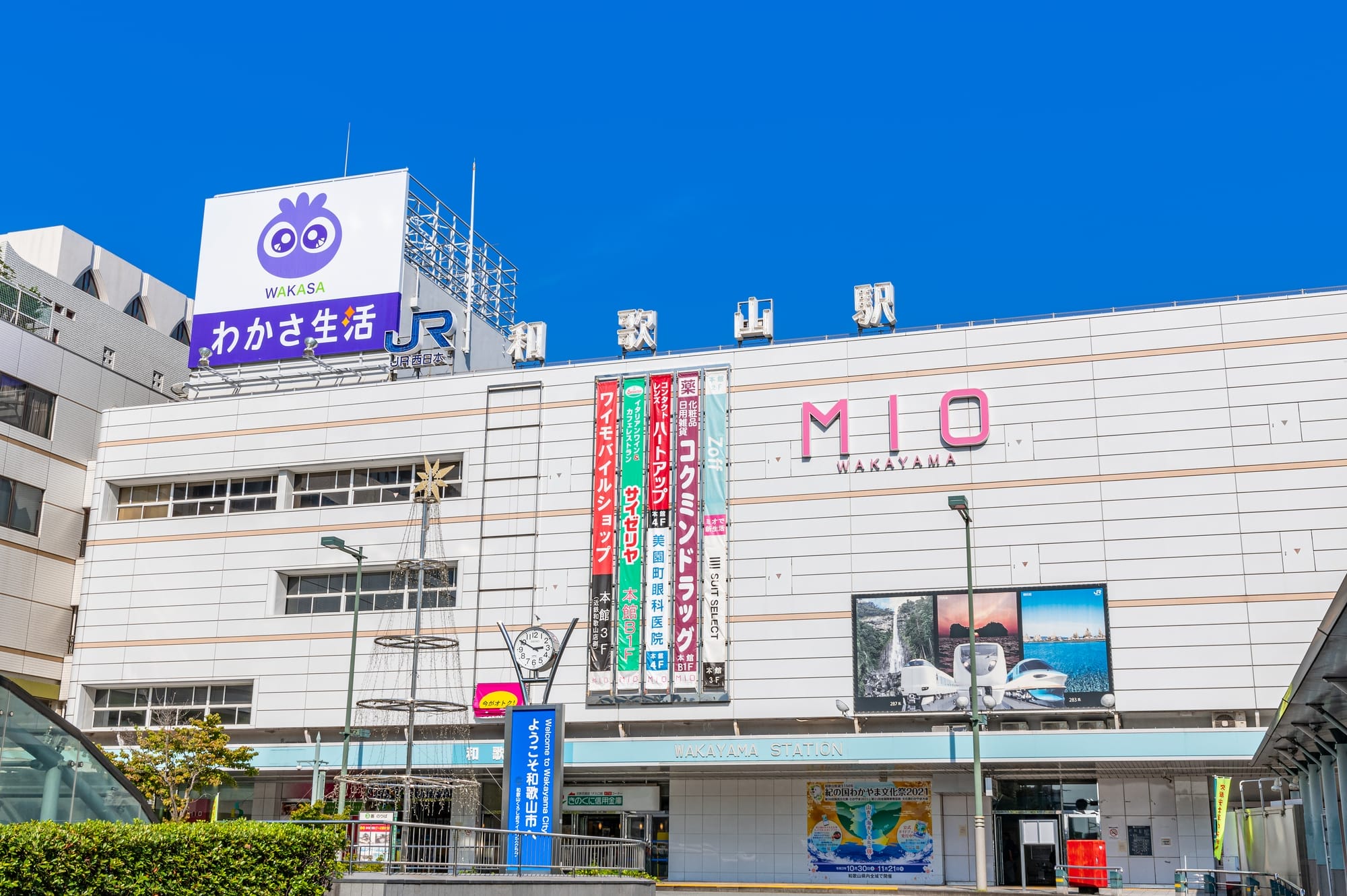 大きなMIO和歌山の看板と様々な店舗、そして真っ青な空を背景にした和歌山駅ビル。.
