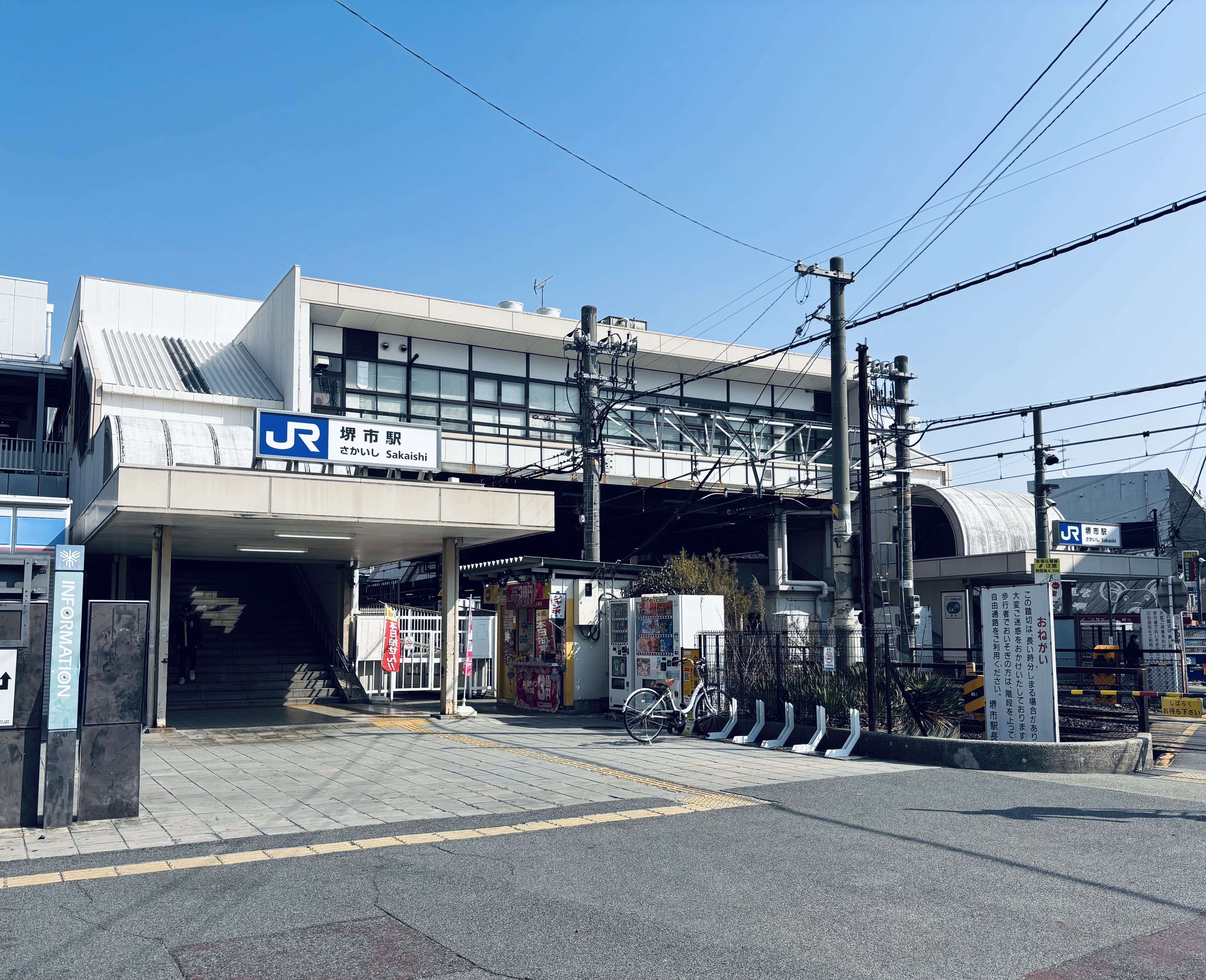 画像は日本のJR桜井駅の外観で、澄み切った青空の下、駅の入り口、駐輪場、線路が描かれている。.