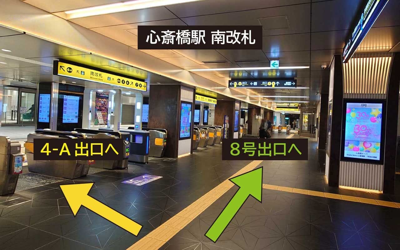 床に4-A出口と8番出口を示す矢印がある日本の地下鉄駅。改札とデジタル表示が見える。.