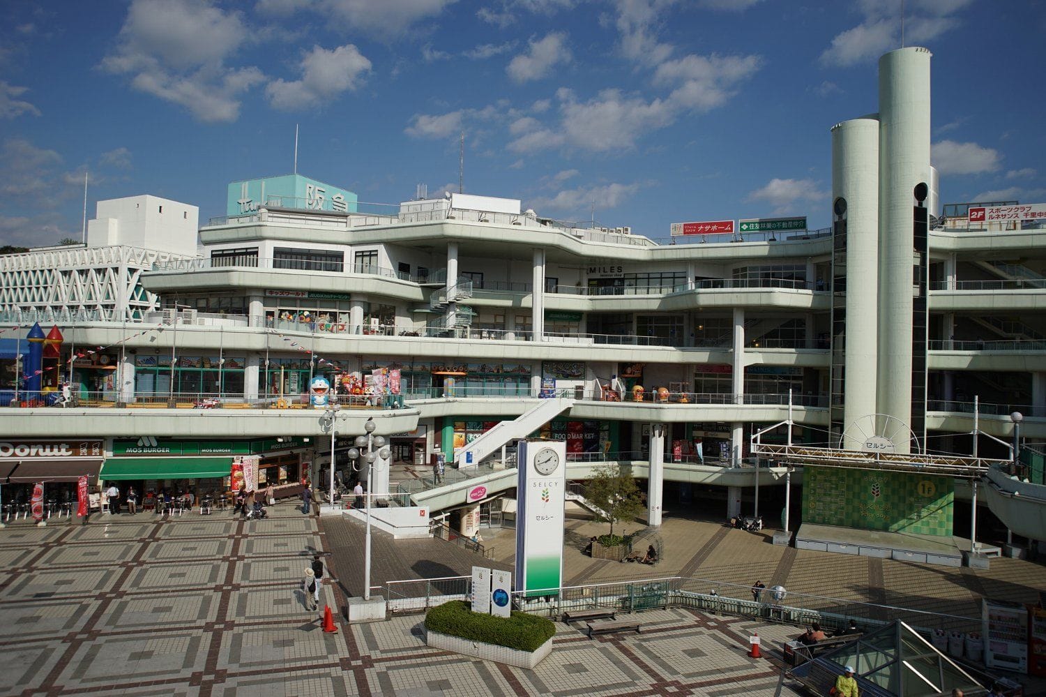 一部曇り空の下、屋外通路、店舗、模様タイルの広場がある複合ショッピングセンター。.