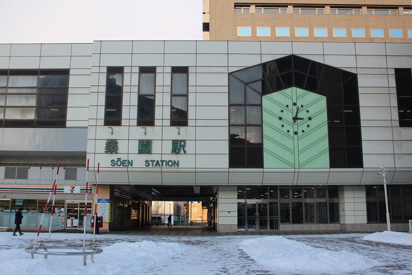 大きな時計の文字盤を持つ近代的な駅舎が雪に囲まれている。.