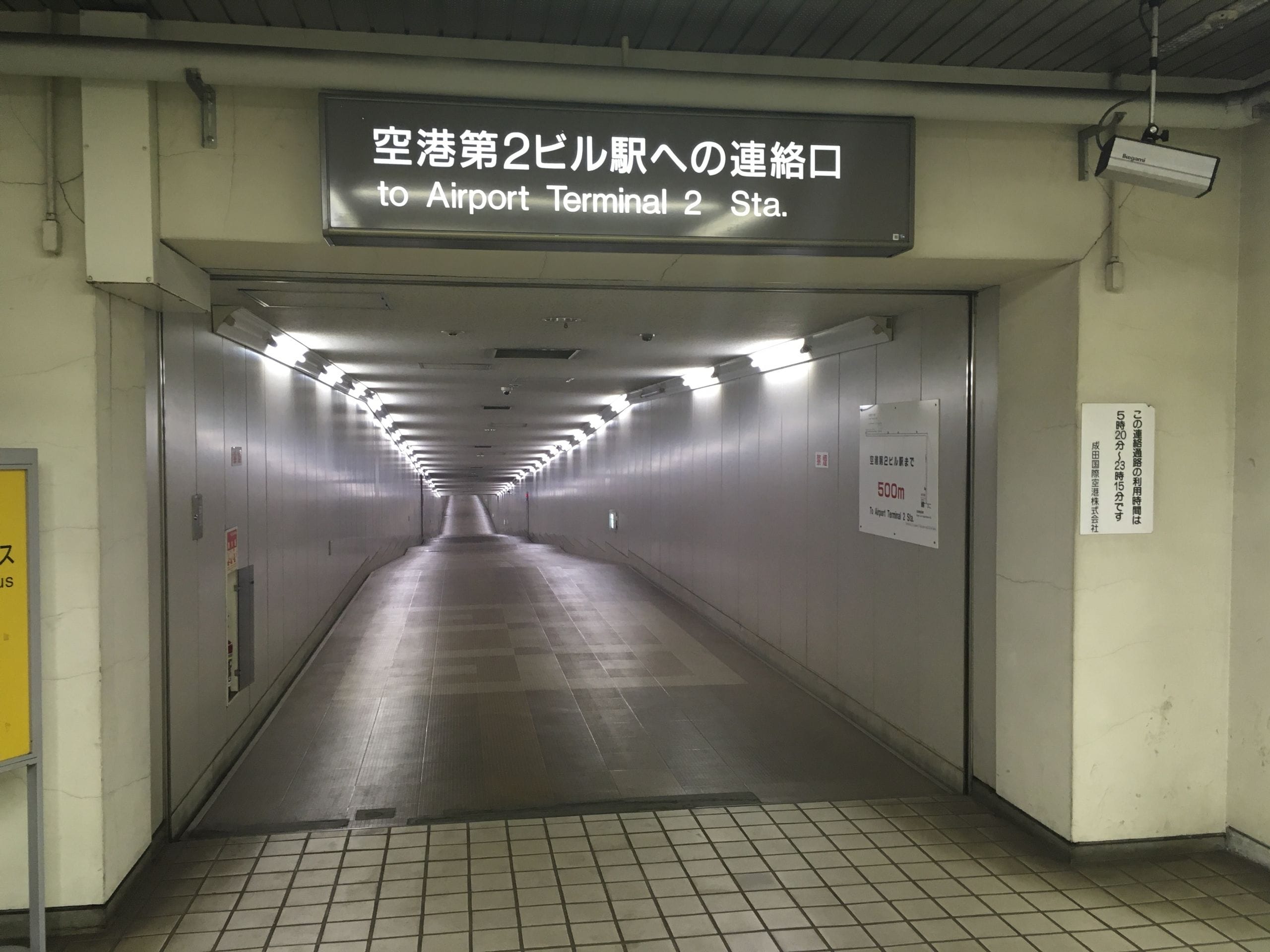 明るい地下通路の頭上には、空港第2ビル駅への案内板が日本語と英語で設置されている。.